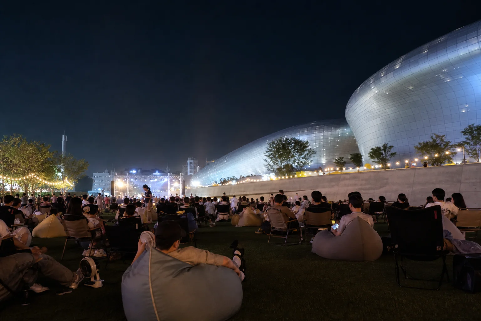 An original editorial illustration of visitors seated outdoors near DDP at night