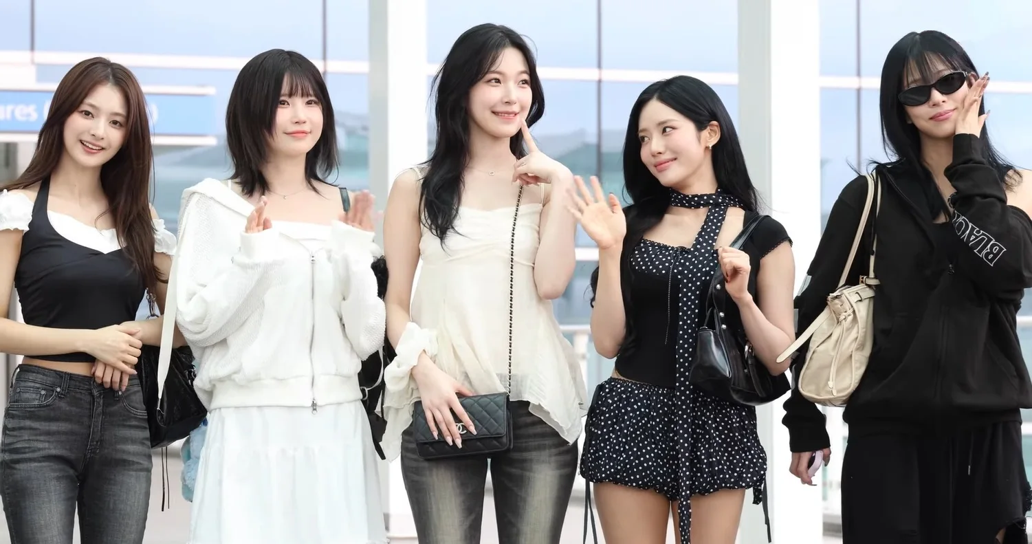 The five members of fromis_9 posing together at an airport in August 2025
